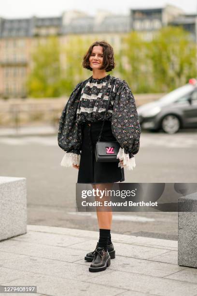 Marta Cygan wears a gray floral print ruffled top with puff sleeves and lace, a black skirt, a black leather Vuitton bag with neon pink logo, black...