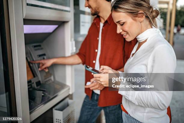 young couple using atm machine to withdraw money from credit card - man atm smile stock pictures, royalty-free photos & images