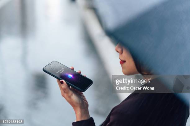 woman using voice assistant on smartphone in the rain - copilot ストックフォトと画像
