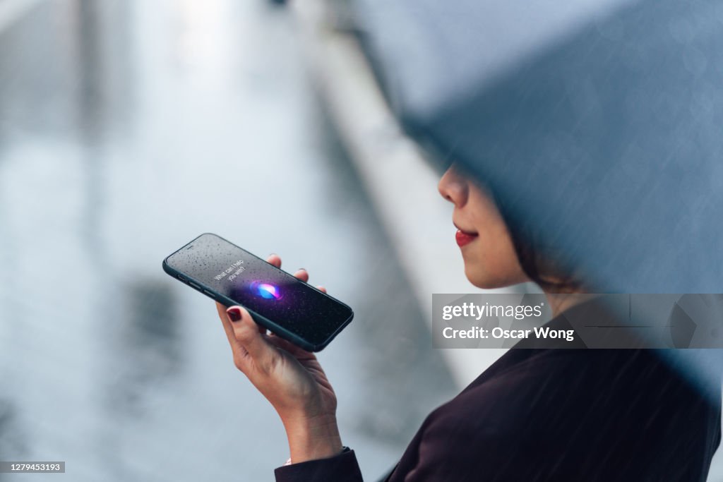 Woman using voice assistant on smartphone in the rain