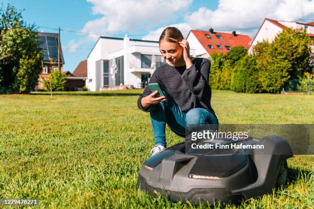 ung kvinna som kontrollerar robotgräsklippare i sommarträdgård - gräsklippning bildbanksfoton och bilder