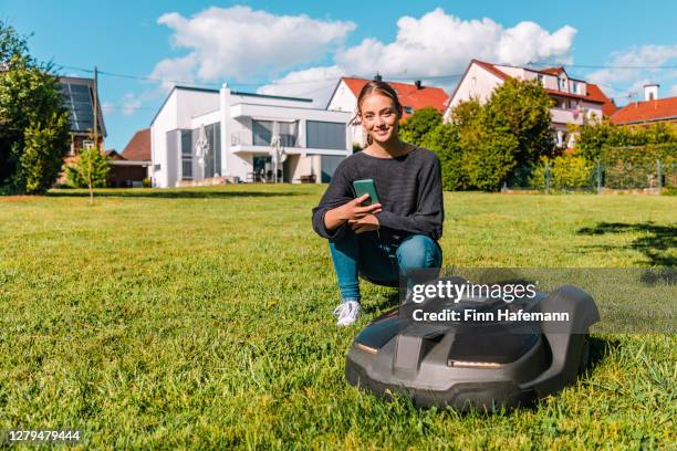 robotic lawn mower programmed with mobile phone app by a smiling woman - mower stock pictures, royalty-free photos & images