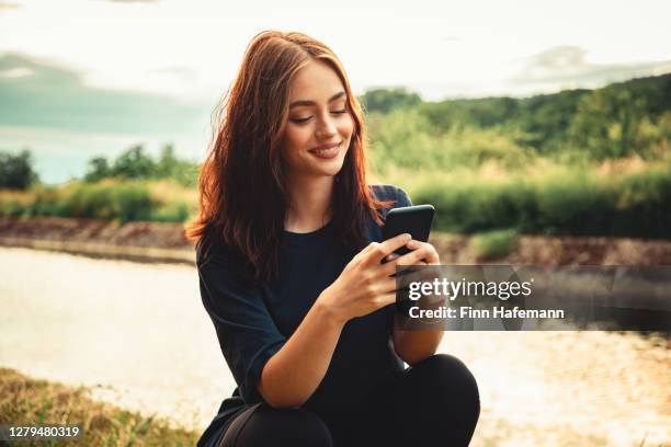 happy smiling young woman writing messages on her smartphone - woman smartphone nature stock pictures, royalty-free photos & images