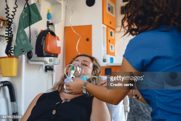 young female nurse with face mask helping a patient with respirator in ambulance during pandemic - respiratory disease stock pictures, royalty-free photos & images
