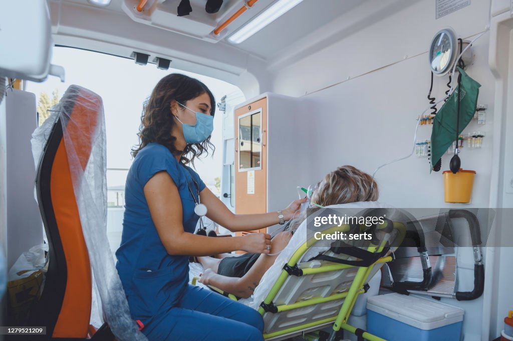 Young female paramedic with face mask helping a patient with respirator in ambulance during pandemic