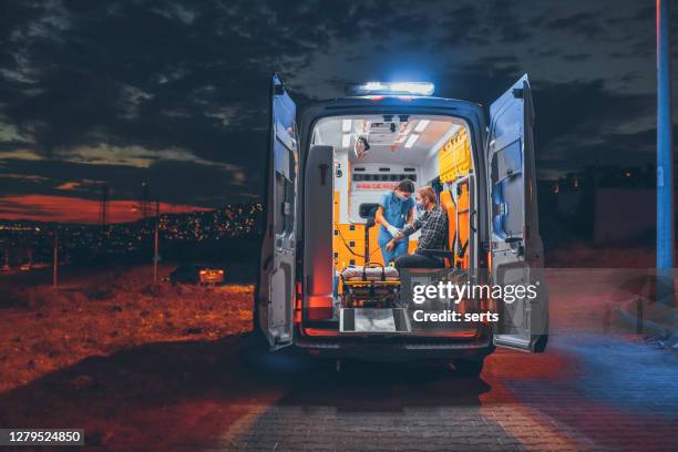 female paramedic with face mask helping a patient and measures patient’s blood pressure in ambulance during pandemic - ambulance imagens e fotografias de stock