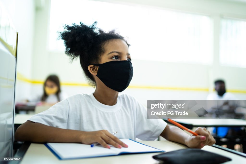 Schoolgirl wearing face mask studying in classroom