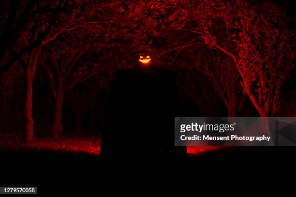 mysterious hooded man holds in hands illuminated spooky jack o' lantern during halloween - jack o lantern imagens e fotografias de stock