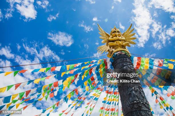 garuda sitting on a totem pole and tibetan buddhism prayer flags against blue sky - flagpole sitting stock-fotos und bilder