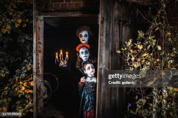 three kids in spooky halloween costumes standing in door of barn - halloween zombie makeup stock pictures, royalty-free photos & images