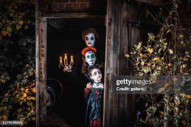 three kids in spooky halloween costumes standing in door of barn - vampire family imagens e fotografias de stock