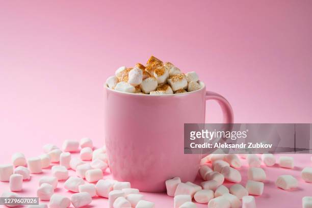 a cup of hot cocoa or coffee with marshmallows sprinkled with cinnamon spices on a bright pastel pink background. small airy meringues are scattered nearby. - hot chocolate stock pictures, royalty-free photos & images