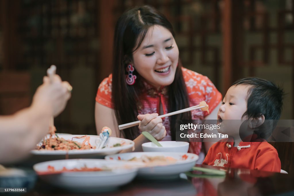 Asian chinese mother feeding her son during family chinese new year reunion dinner with traditional dishes raw fish lau sang