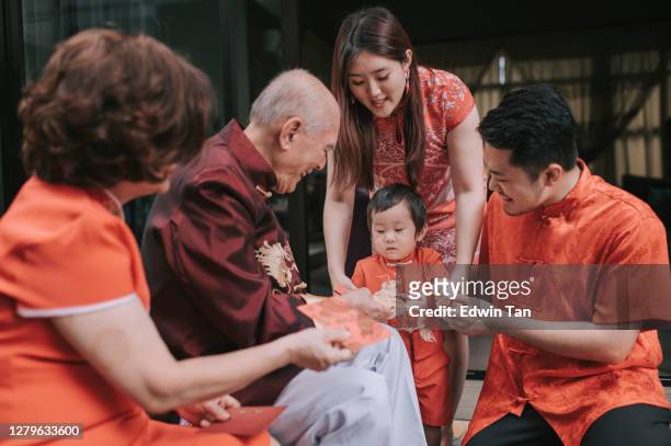 asian chinese family senior grandparent giving red packet ang pao to grandson after chinese new year reunion dinner having traditional dishes raw fish lau sang - respect stock pictures, royalty-free photos & images