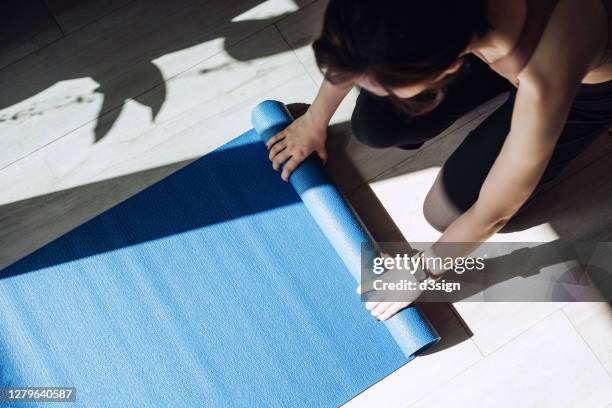 overhead view of young asian sports woman practicing yoga / exercising at home. unrolling yoga mat, getting prepared to work out in the fresh bright morning - colchoneta de ejercicio fotografías e imágenes de stock