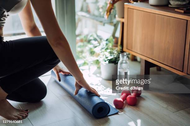 close up of young asian sports woman practicing yoga / exercising at home. unrolling yoga mat, getting prepare to work out in the fresh bright morning - sport equipment stock-fotos und bilder