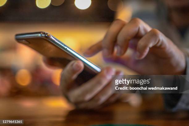 closeup image of a man holding and using smart phone with coffee cup on wooden table in cafe - smartphone in hand stockfoto's en -beelden