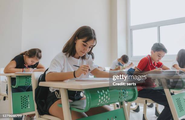 bambini concentrati seduti alla scrivania a lezione in classe, scrivendo - test foto e immagini stock