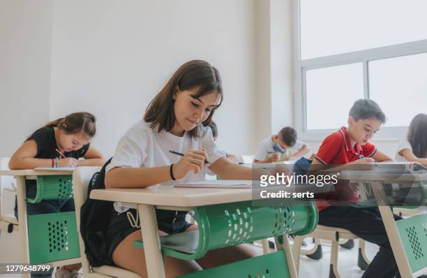 concentrated small school children sitting at the desk on lesson in classroom, writing - schoolboy stock pictures, royalty-free photos & images