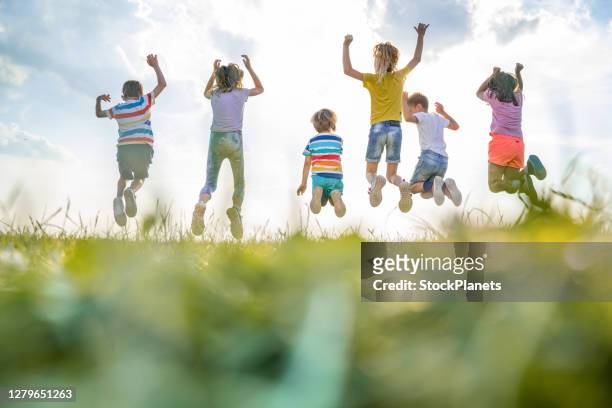 gruppo di vista posteriore di bambini che saltano nella natura - divertirsi foto e immagini stock