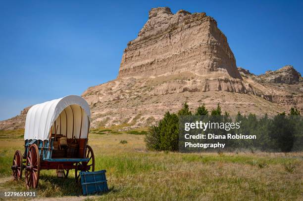 covered wagon in front of a large butte in scottsbluff, nebraska - planwagen stock-fotos und bilder