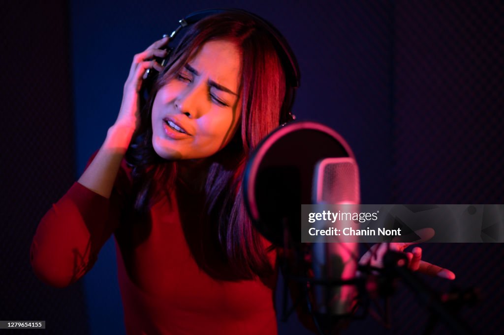 Beautiful young woman singing behind the microphone at a recording studio and looking very happy