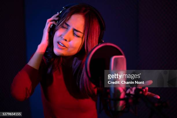beautiful young woman singing behind the microphone at a recording studio and looking very happy - pop musician stock pictures, royalty-free photos & images