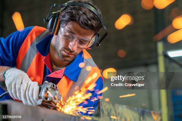 the smart engineer working and wearing protection wear with electric grinder tool on steel structure in factory, sparks flying. - kreissäge stock-fotos und bilder