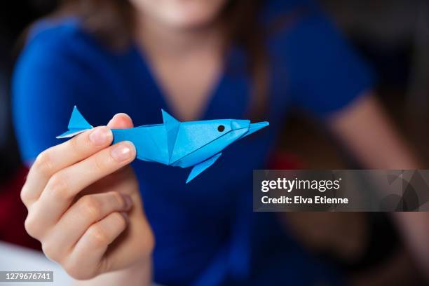 teenager holding homemade origami sculpture of a dolphin made from blue paper - animaux origami photos et images de collection