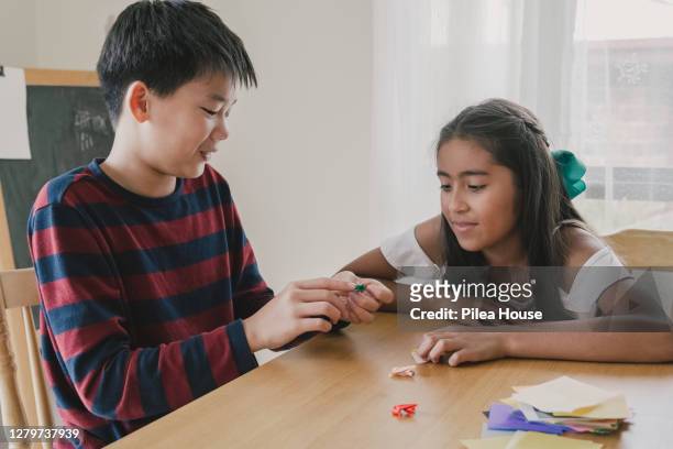mixed race preteen boy and girl making origami frog, kid art and craft - origami instructions stock pictures, royalty-free photos & images