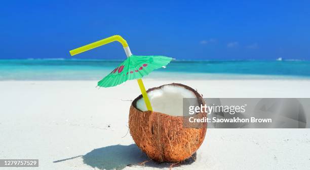 a coconut juice with a straw and an umbrella by the beach - cocktail umbrella stock pictures, royalty-free photos & images