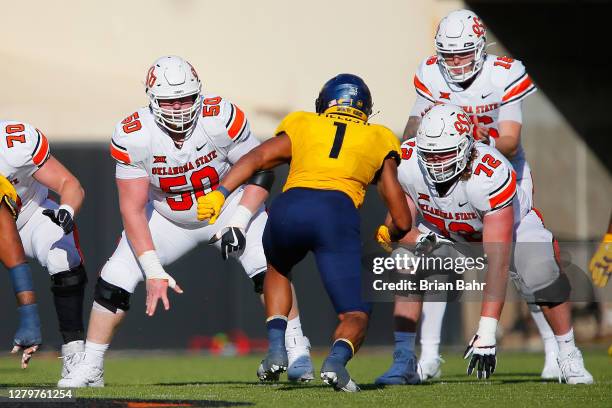 Center Ry Schneider and offensive lineman Josh Sills of the Oklahoma State Cowboys block linebacker Tony Fields II of the West Virginia Mountaineers...