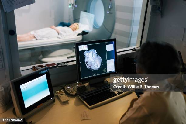 doctor watching from computer desk as patient enters mri scanner - mri technician fotografías e imágenes de stock