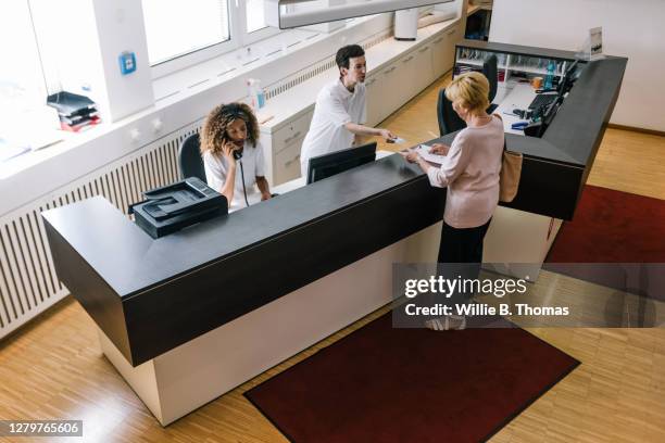 receptionist handing medical insurance card back to patient at mri clinic - medical lobby stock pictures, royalty-free photos & images