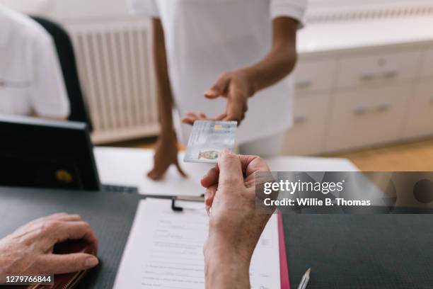 woman handing receptionist medical insurance card at mri clinic reception - medical insurance stock-fotos und bilder