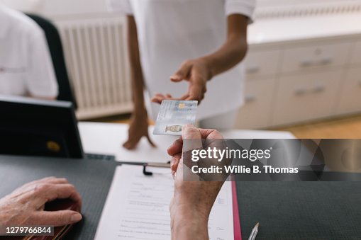 Woman Handing Receptionist Medical Insurance Card At MRI Clinic Reception Woman Handing Receptionist Medical Insurance Card At MRI Clinic Reception