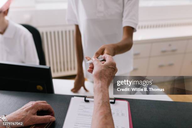 mature woman handing medical insurance card to clinic receptionist - arzthelferin stock-fotos und bilder