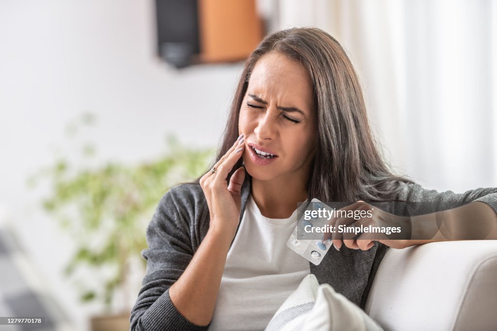 Intensive toothache of a woman holding pills blister.