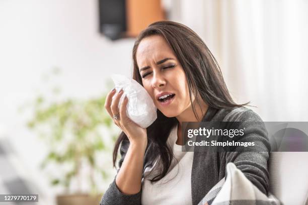 toothache of a young female holding a pack of ice on her cheek. - toothache stock pictures, royalty-free photos & images