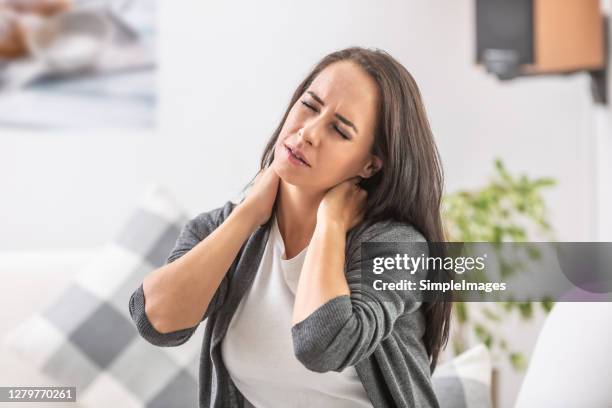 neck pain of a young woman sitting at home. - cramp stock pictures, royalty-free photos & images