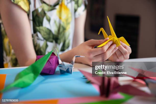 teenager making a yellow origami paper crane - origami a forma di gru foto e immagini stock