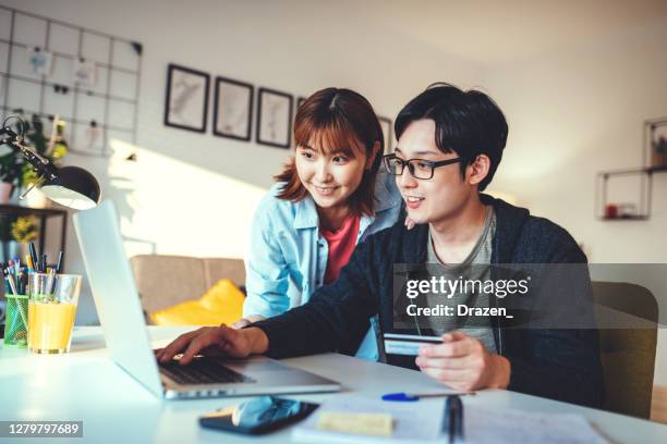 pareja japonesa en casa, usando internet para pedir bienes, pagando con tarjeta de crédito - pedir matrimonio fotografías e imágenes de stock