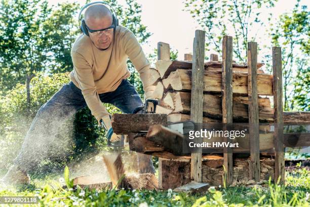 man on sunny spring day preparing firewood for winter - chainsaw stock pictures, royalty-free photos & images