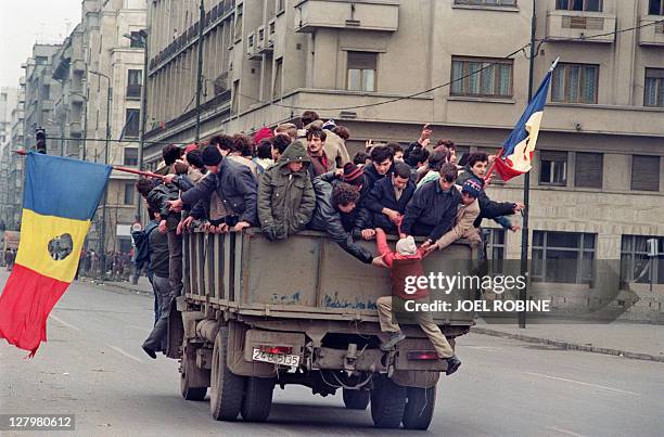 Romanian civilians cross Bucharest on a truck waving flags where the communist symbol has been cut off on December 24, 1989 as the anti-Communist...