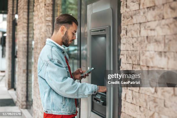 argent de retrait de jeune homme d’un distributeur de billets de banque - dab photos et images de collection