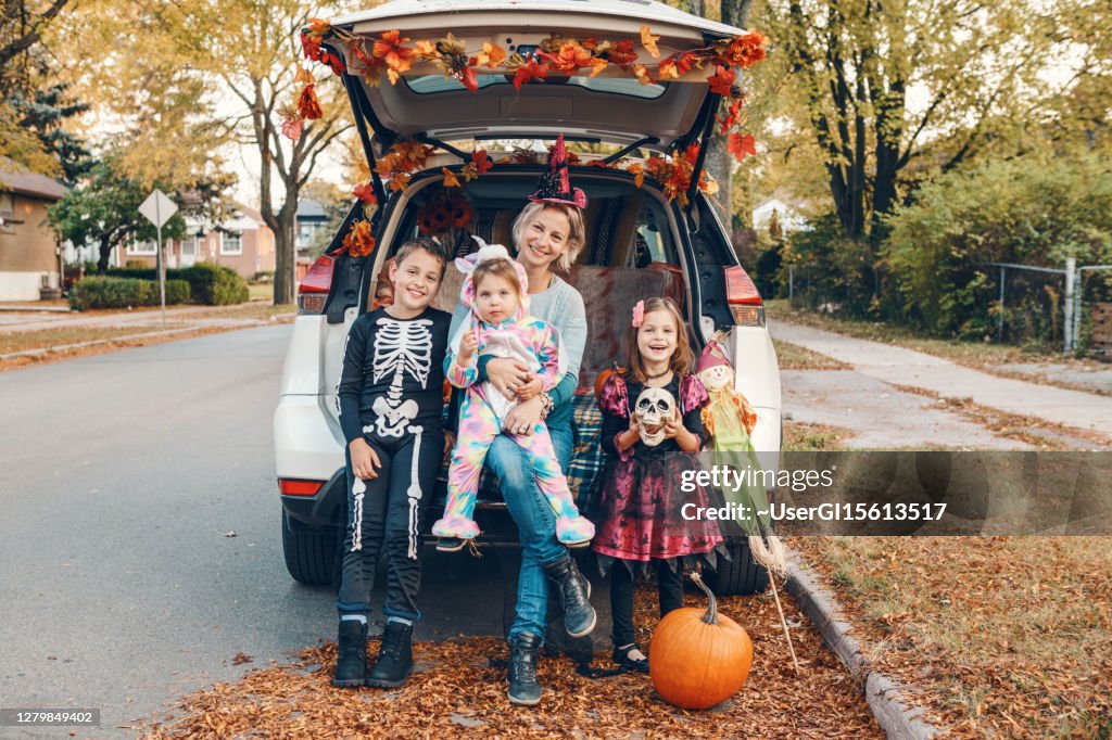 Trick or trunk. Family celebrating Halloween in trunk of car. Mother with three children kids celebrating traditional October holiday outdoors. Social distance and safe alternative celebration.