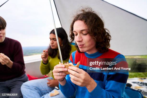 teenage man tucking in to has sandwich while camping with friends - hungry teen stock pictures, royalty-free photos & images