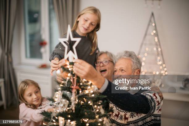 glückliche familie schmückt einen weihnachtsbaum mit ornamenten - christmas family tree stock-fotos und bilder