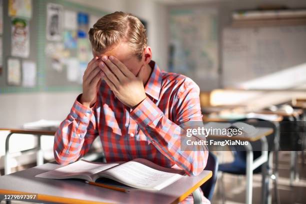 stressed male student sitting with book at desk - adhs stock pictures, royalty-free photos & images