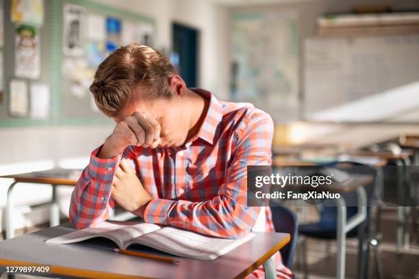 estudiante masculino estresado sentado con libro en el escritorio - failure fotografías e imágenes de stock